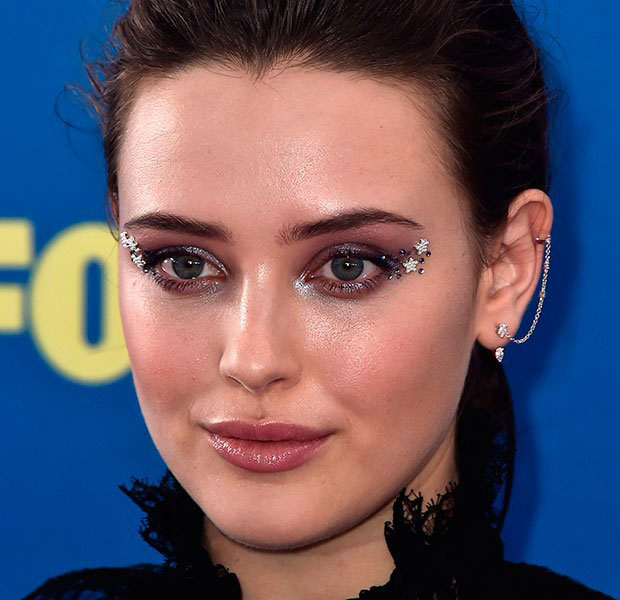makes-halloween-famosas-Katherine-Langford Katherine Langford posando para foto com make brilhante em tons de rosa e brilhos em formato de estrela no canto do olho