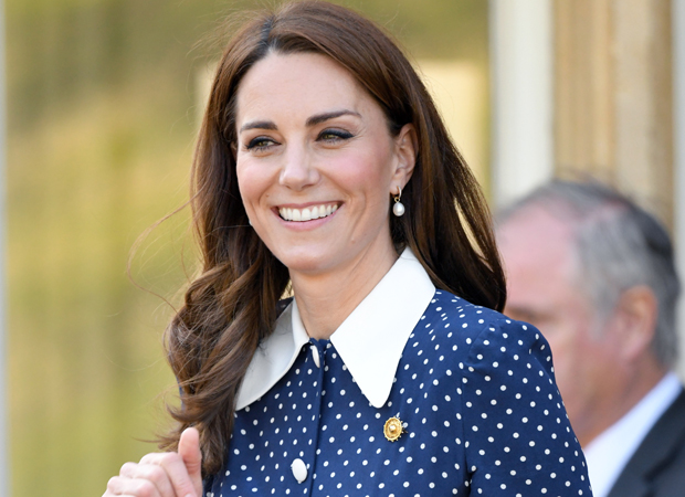 Kate Middleton sorrindo; ela usa uma camisa azul com bolinhas brancas com gola branca