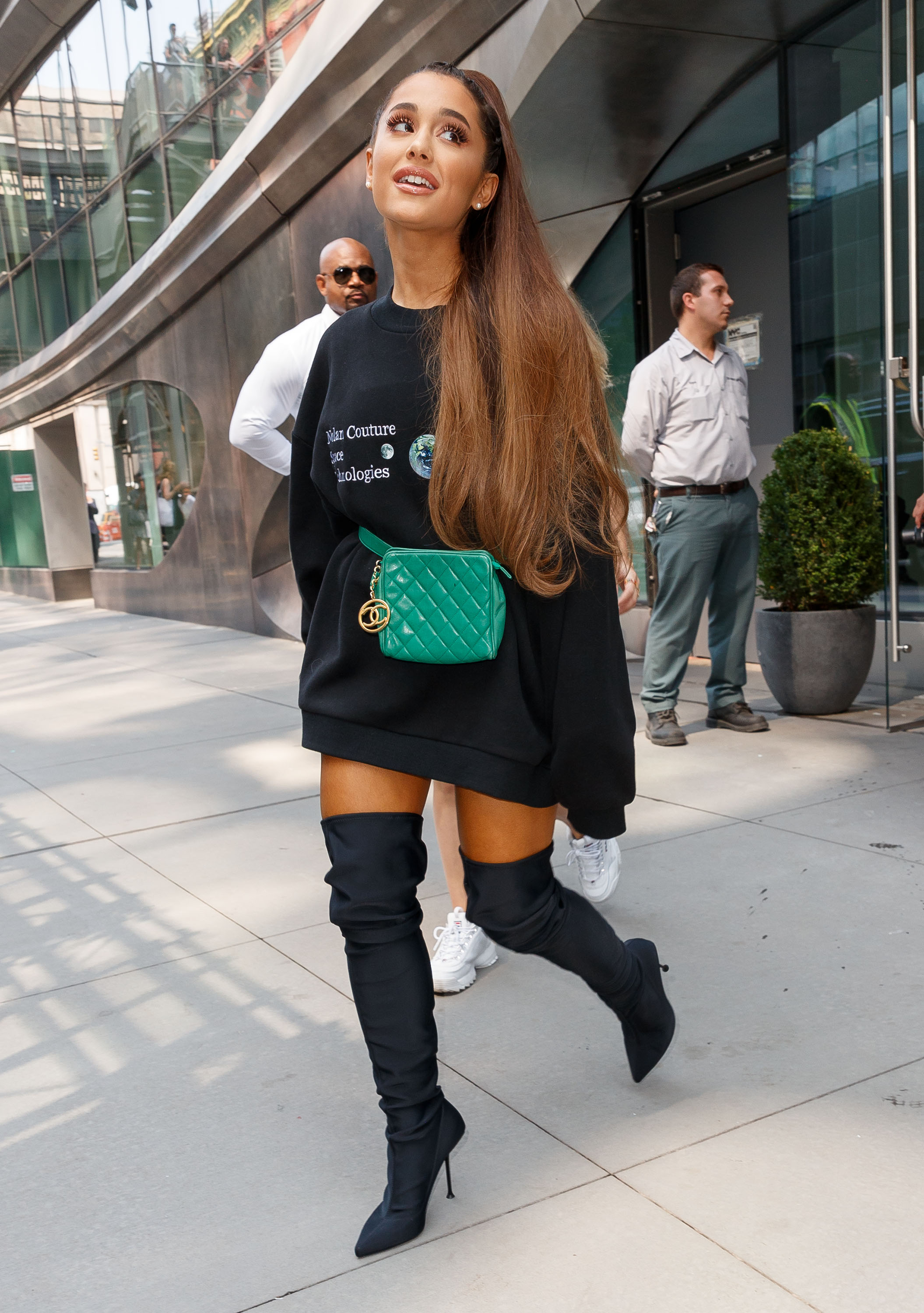 ariana-grande-moletom Ariana Grande usando moletom preto oversized com pochete verde e bota over the knee preta.