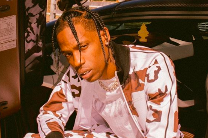 Travis Scott posando para foto com corpo curvado e roupa branca com detalhes em marrom