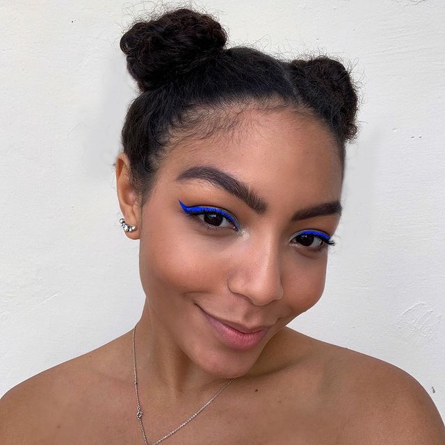 any-gabrielly-penteado-space-buns Selfie da cantora Any Gabrielly com foco no rosto e penteado. Ela usa uma maquiagem natural com delineado gatinho azul e cabelo preso no penteado space buns (dois coques altos). Ela olha para a câmera e sorri levemente.