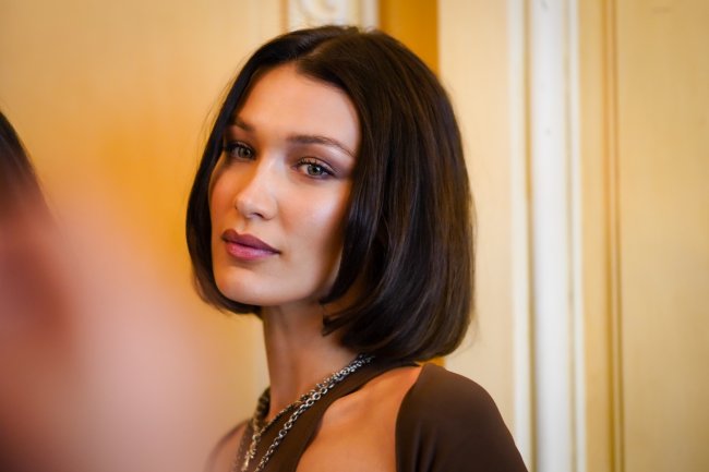 Foto de Bella Hadid com cabelo curto moreno, roupa marrom.