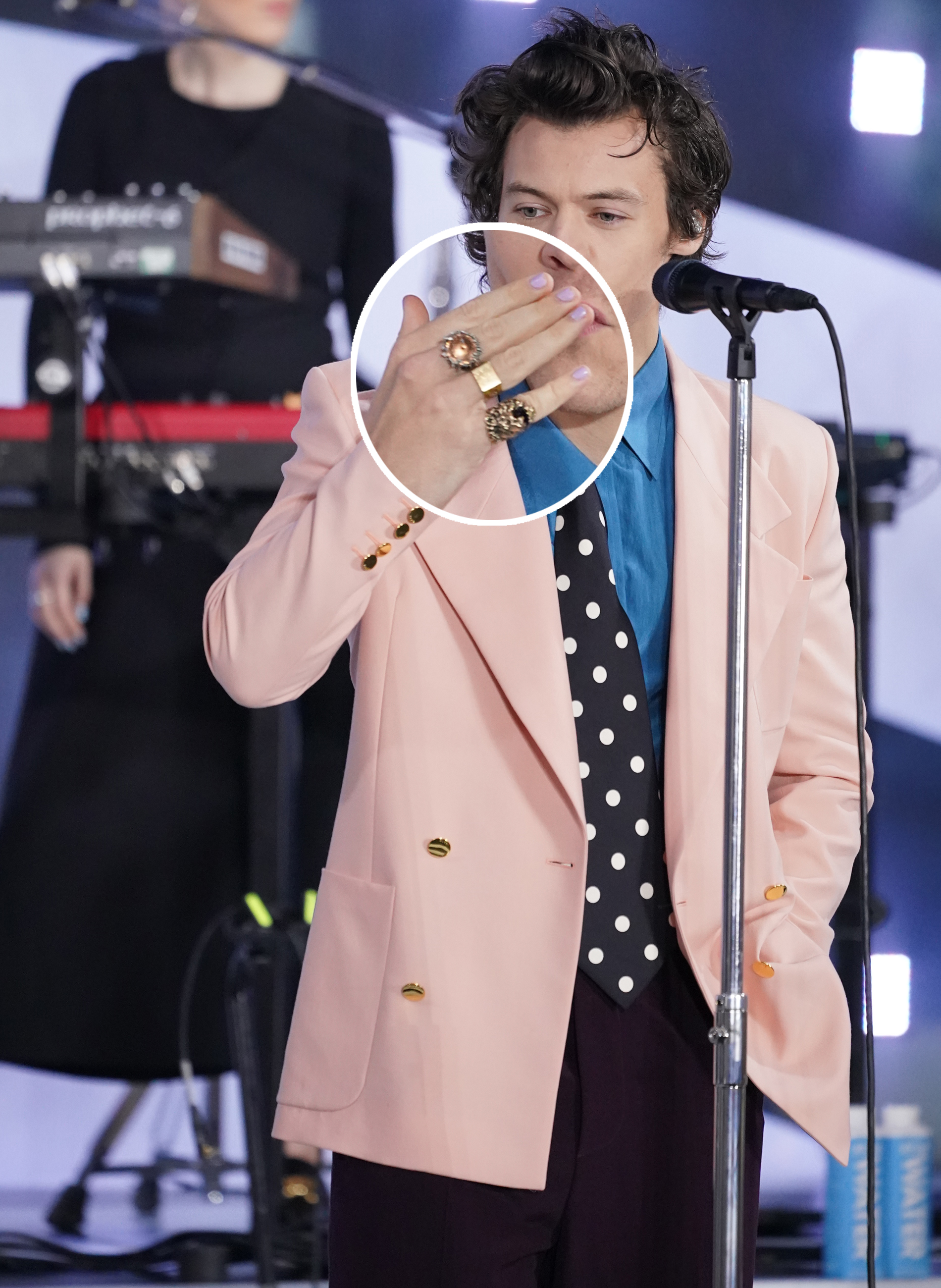 Harry Styles esmalte lavanda3 Harry Styles usando blazer rosa com gravata preta de poá, camisa azul e mix de anéis nos dedos. Ele está com a mão na boca mandando beijo para o público.