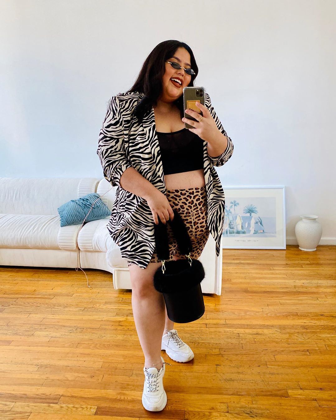 biker-shorts-Jessica-Torres Garota usando top faixa preto com bermuda ciclista com estampa de oncinha, blazer com estampa de zebrinha. Ela está em frente ao espelho, sorrindo, com um óculos de sol, segurando uma bolsa preta e usando tênis branco.