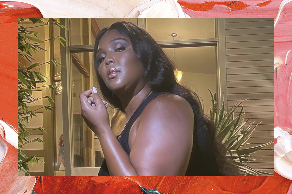 Lizzo Lizzo posando para foto; a cantora está de lado olhando para câmera com roupa preta e expressão séria, uma de suas mãos está levantada perto do rosto e sua unha está pintada de branco