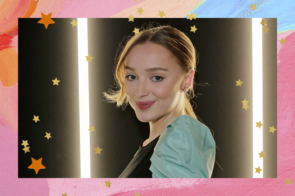 A atriz Phoebe Dynevor está com cabelo preso em um rabo baixo e um leve sorriso com os lábios, sem mostrar os dentes