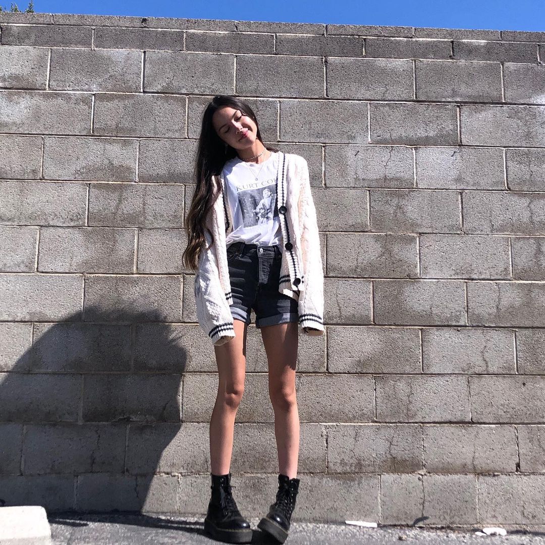 4 Olivia Rodrigo usando short e coturno pretos, camiseta branca e casaco bege