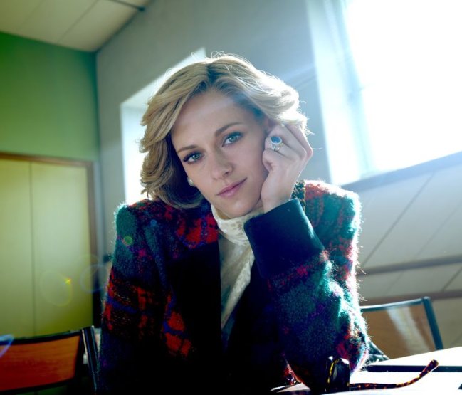 kristen-stewart-spencer-princess-diana-1616683385 Kristen Stewart como Princesa Diana, com os cabelos soltos, uma mão sob a bochecha, vestindo um blazer estampado vermelho azul e verde