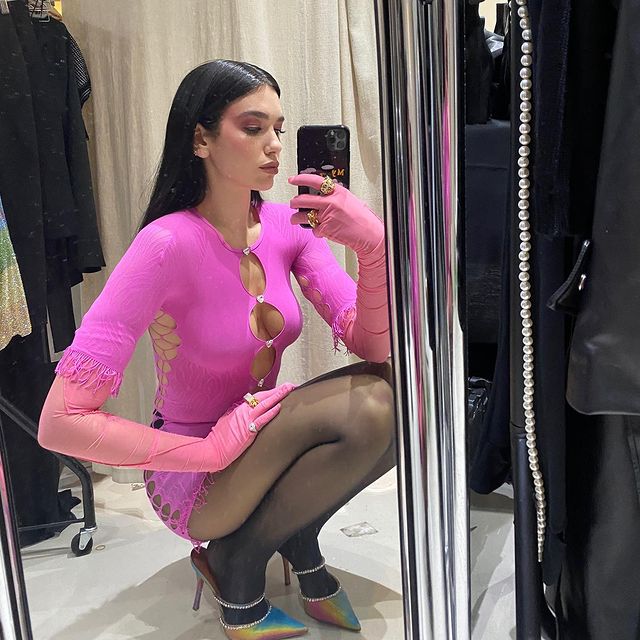 Dua Lipa usando vestido rosa com recortes circulares na região do colo, dos seios e da barriga