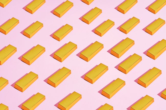 Como guardar dinheiro desde cedo pode ajudar a adolescente a longo prazo Ilustração de várias barrinhas de ouro em cima de um fundo rosa claro