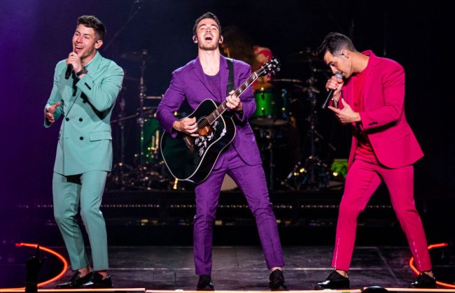 crushes vestindo calça curte que vão te fazer ver a peça com outros olhos Jonas Brothers se apresentando em Detroid com a turnê Happiness Begins; o Nick veste um conjunto azul turquesa, o Kevin um roxo e o Joe um pink