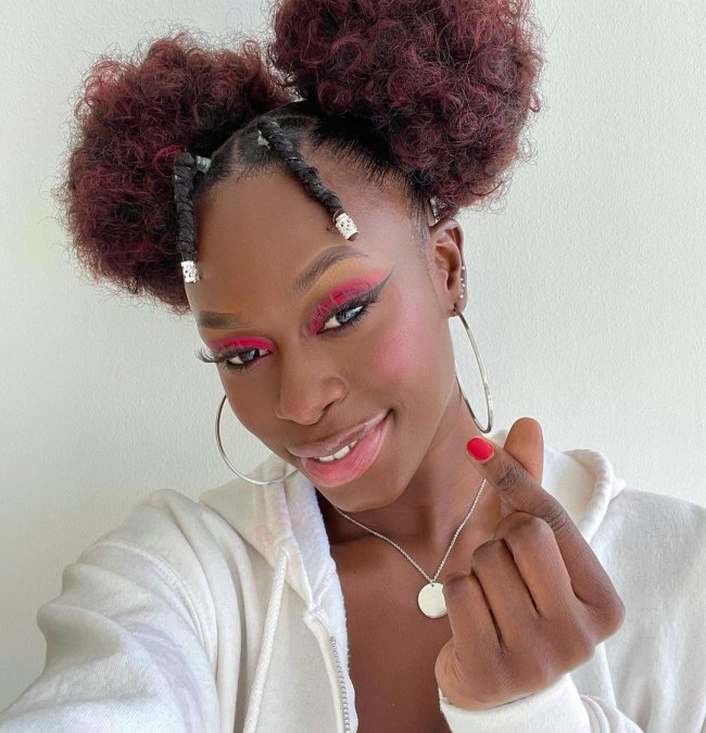 Diarra Sylla do now united posando para foto com sombra vermelha, e cabelo preso em dois coques laterais, usando uma blusa de moletom branca.