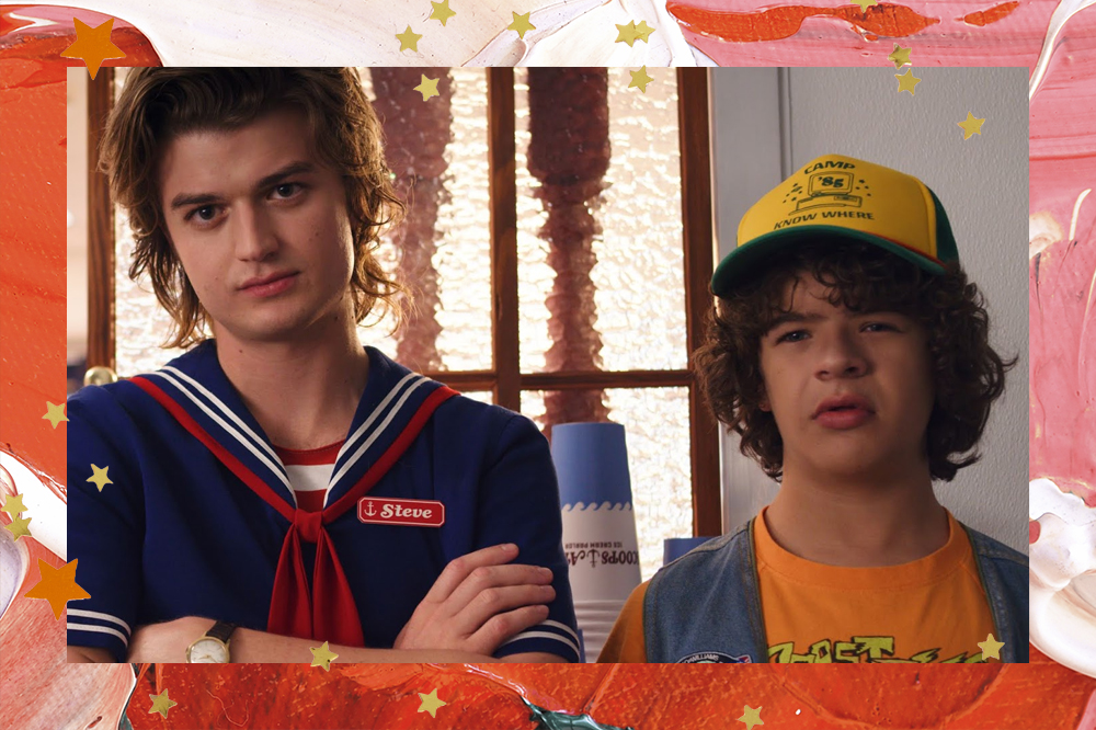 Steve e Dustin, de Stranger Things, um ao lado do outro. Steve com os braços cruzados e Dustin com expressão confusa