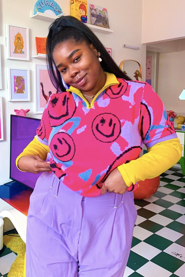 Look colorido com smile Jovem com as mãos no bolso, usando camisa com gola amarela e cor de rosa com smiles pretos, calça lilas e blusa amarela por baixo.