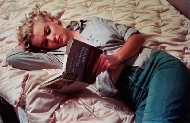 Marilyn Monroe aparece deitada e segurando um livro