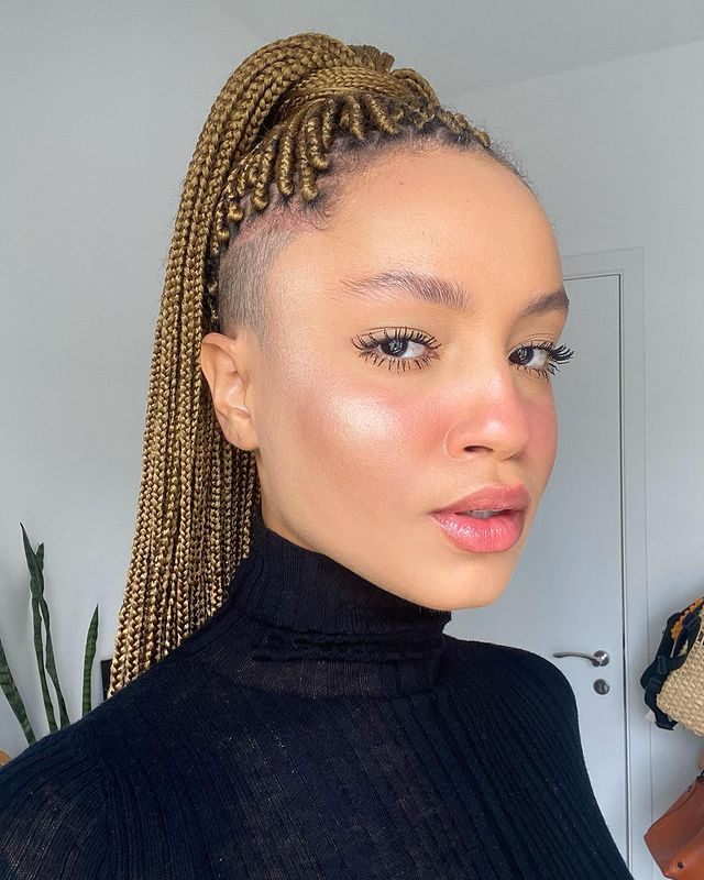 maquiagem-natural-prettamesmo Garota com expressão facial séria com cabelo em tranças preso no topo da cabeça e blusa preta de gola alta