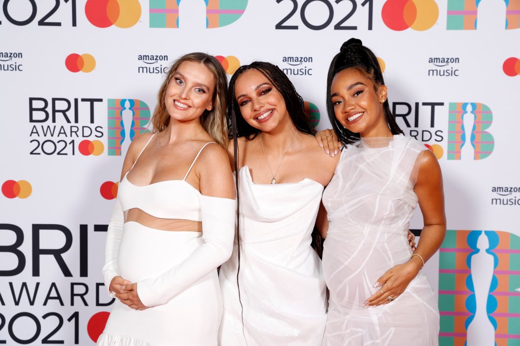 Perrie Edwards, Jade Thirlwall e Leigh-Anne Pinnock, do Little Mix, no BRIT Awards 2021. Perrie, à esquerda, está sorrindo, usando um vestido longo branco com uma transparência entre a parte de cima e a saia, e as duas mãos na sua barriga de grávida. Jade, ao meio, está com um vestido branco sem alças e sorrindo. Leigh-Anne, à direita, está com um vestido branco levemente transparente, sorrindo, e as duas mãos na sua barriga de grávida.