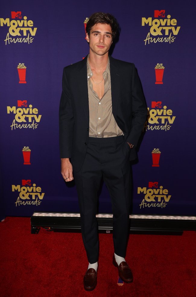Jacob Elordi no MTv Movie & TV Awards Jacob Elordi no MTv Movie & TV Awards, posando com expressão séria no red carpet da premiação usando terno preto e camisa levemente marrom.