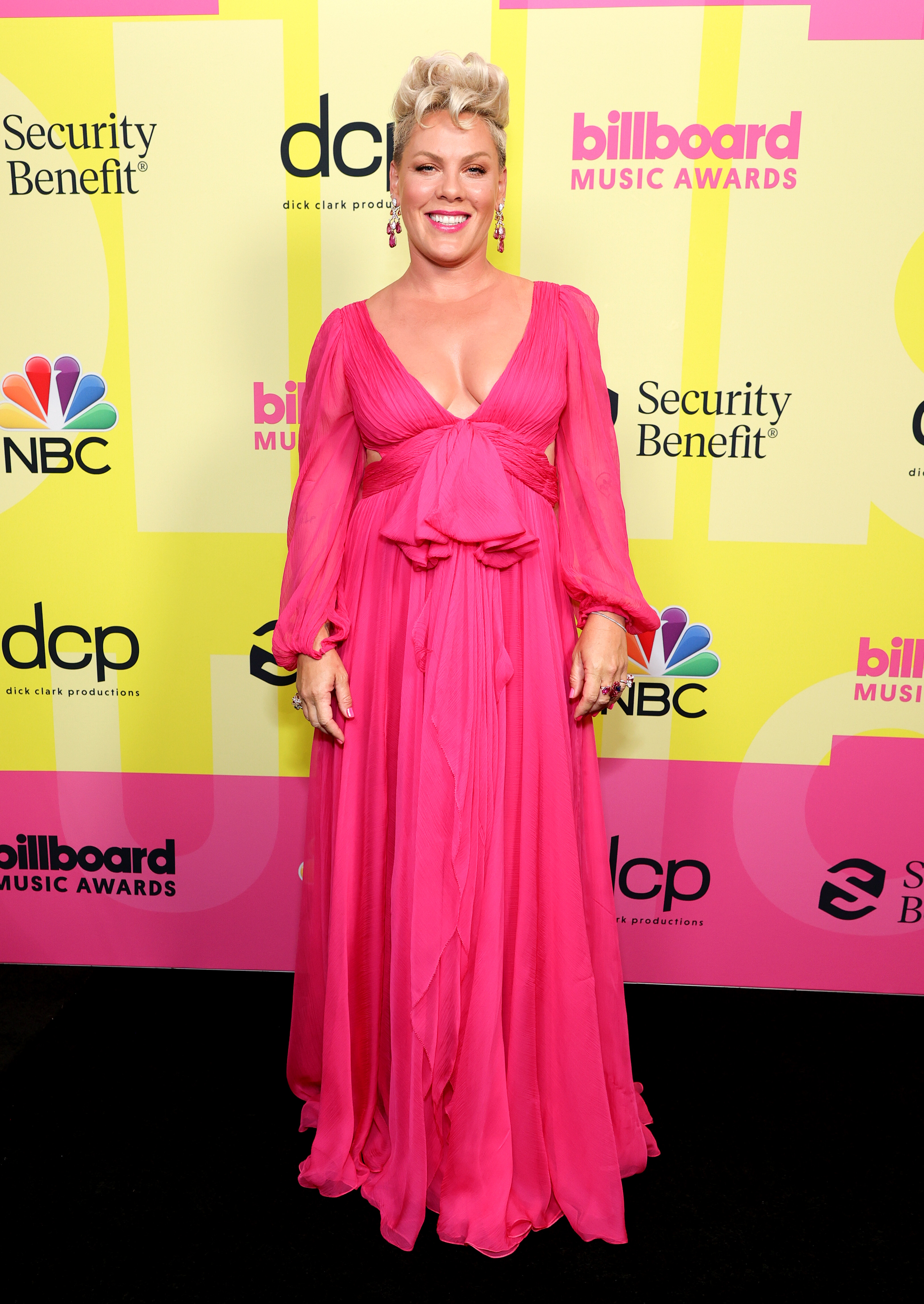 Pink usando vestido longo rosa esvoaçante no Billboard Music Awards 2021. Ela está sorrindo e olhando para a câmera.