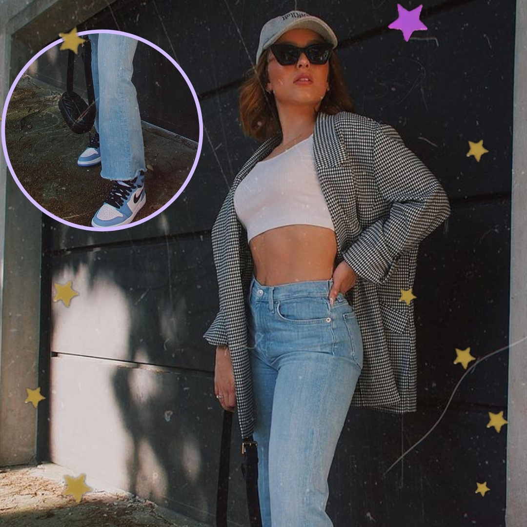 Larissa Manoela com cropped, blazer e boné. A atriz está olhando para cima, com expressão séria, usando óculos escuros e uma de suas mãos está em seu bolso.