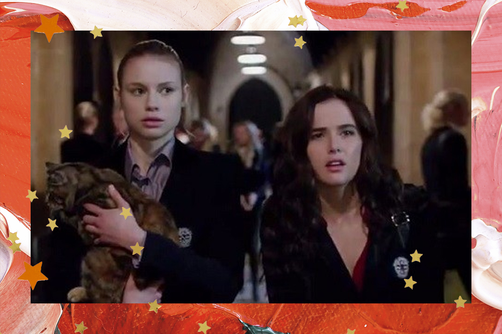 academia de vampiros Lisa e Rose em filme de Academia de Vampiros; Lisa está segurando um gato com expressão surpresa e Rose está fazendo uma expressão confusa ao lado da amiga; as duas estão andando no corredor da escola; a borda da imagem é uma textura de tintas em tons de vermelho, rosa e branco com estrelas amarelas e laranjas como decoração