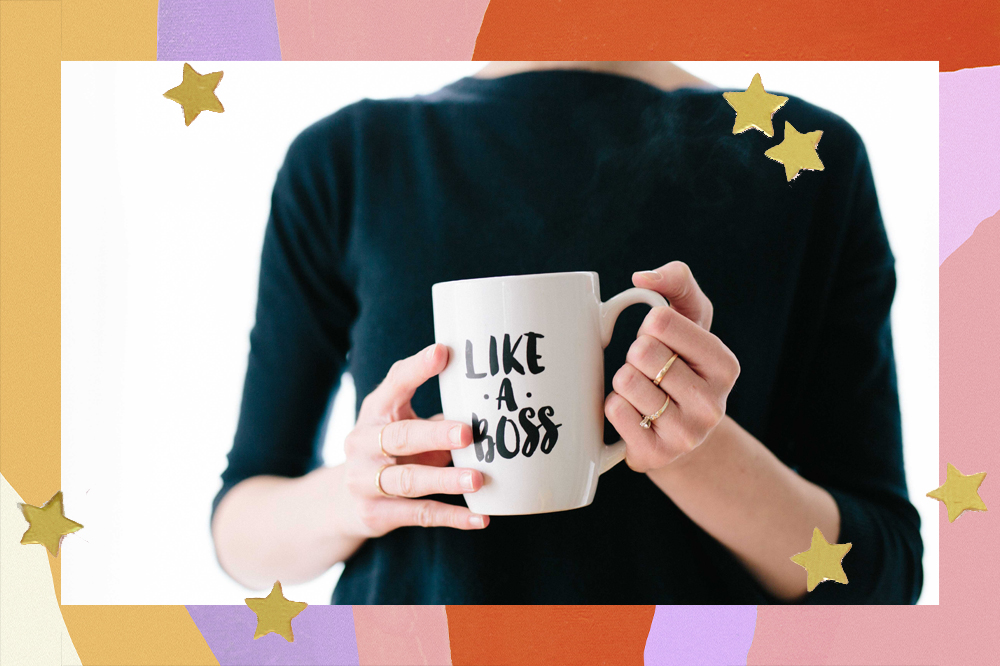 Mulher com anéis e camiseta preta segurando uma caneca branca com os dizeres: "Like a Boss"