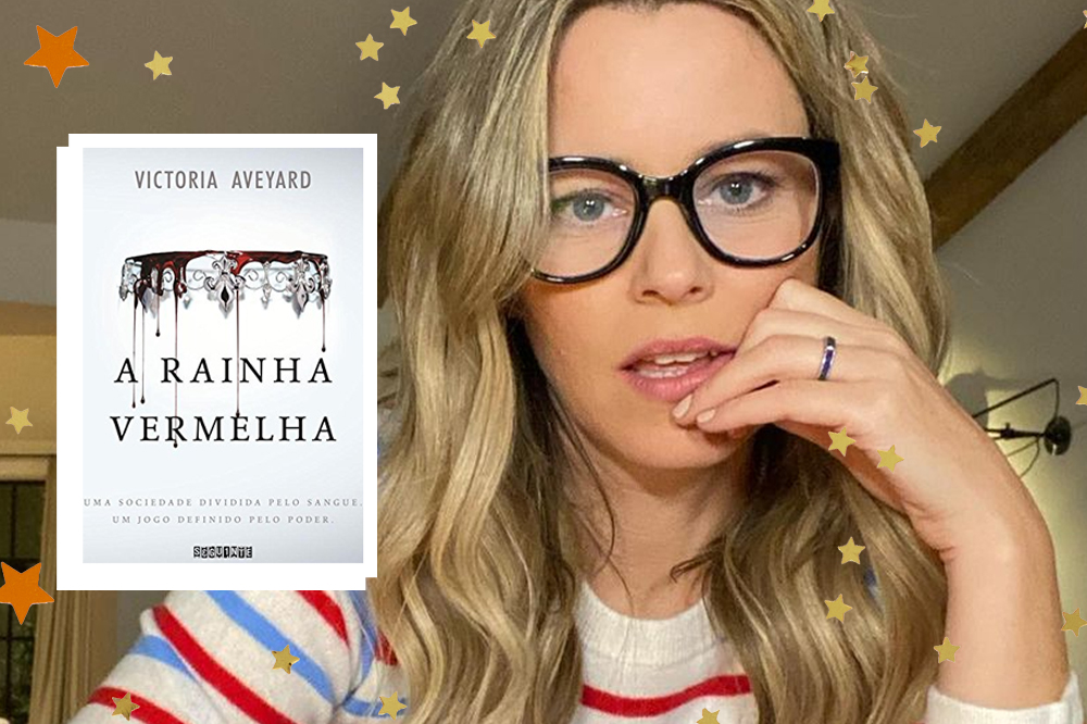 Elizabeth Banks com óculos e blusa com branca com listras vermelhas e azuis; ela está com uma das mãos próxima da boca; ao lado de seu rosto uma colagem da capa do livro A Rainha Vermelha com borda branca e estrelas amarelas e laranjas como decoração