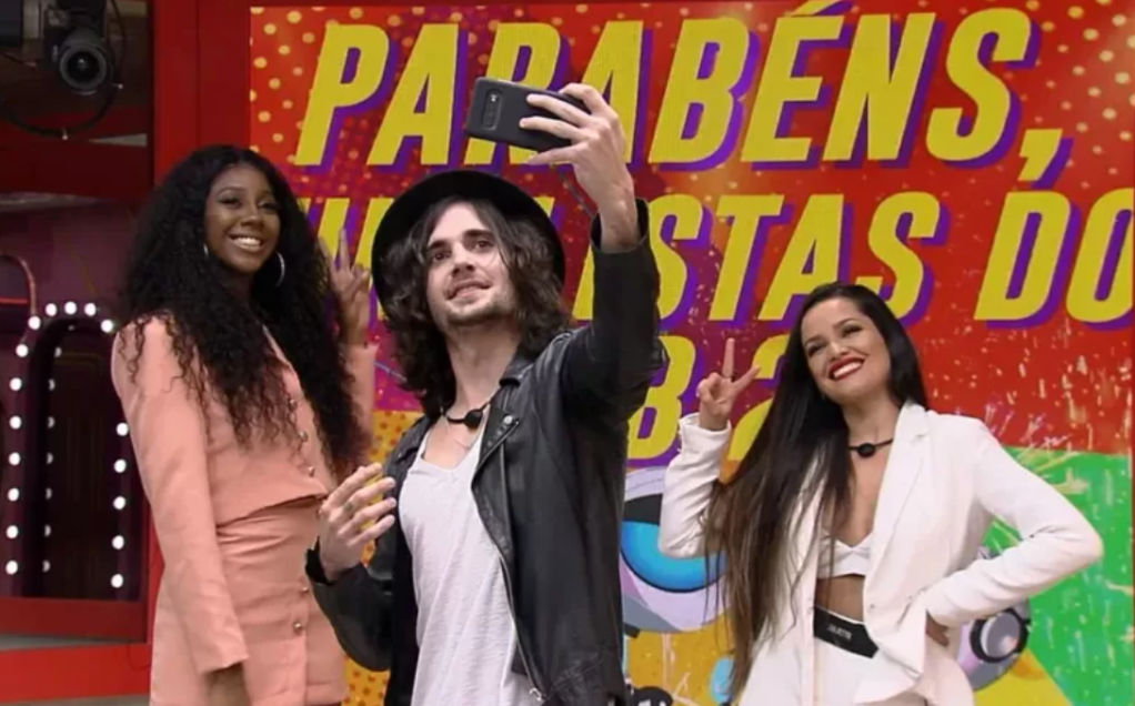 Finalistas do BBB21 posam para uma foto no celular. Ao centro, Fiuk segura o aparelho no alto. À esquerda, Camila posa sorrindo. À direita, Juliette posa sorrindo. Com os dedos indicador e médio ela faz um "V"