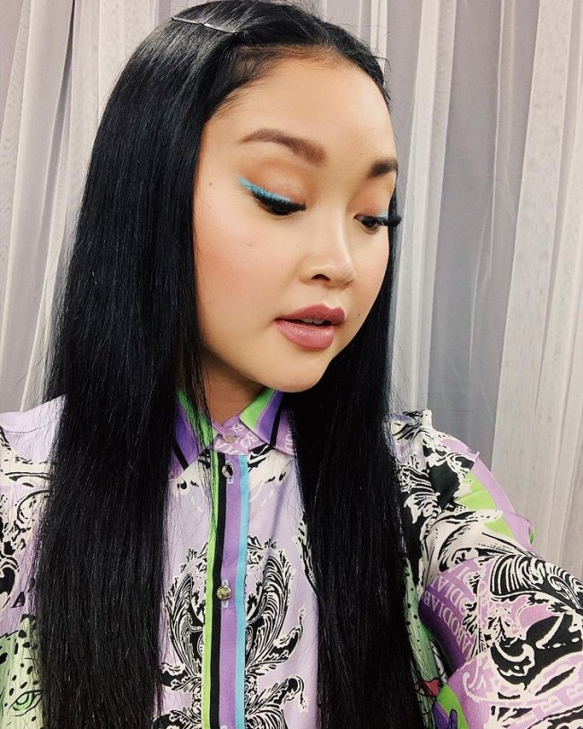 Selfie da atriz Lana Condor. Ela usa um vestido colorido estampado, cabelo solto, delineado azul e pele natural. Ela olha para baixo e não sorri.