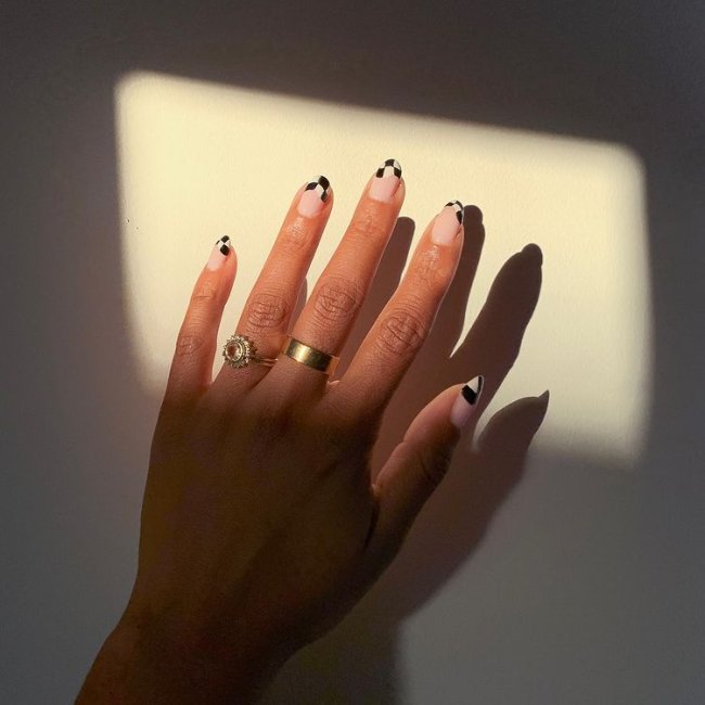 Foto de uma mão com anéis dourados no dedo anelar e médio. Com nail art xadrez preto e branco como francesinha.