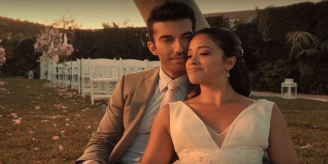 Um casal, durante um casamento, abraçados. Ao fundo o local da cerimônia, com as cadeiras e o altar.