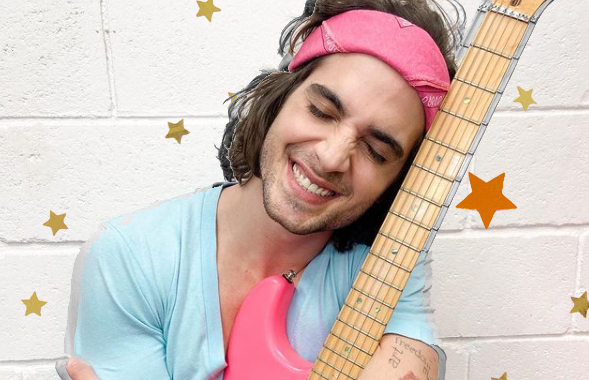 Fiuk abraçando sua guitarra rosa. Ele usa uma bandana rosa no cabelo também