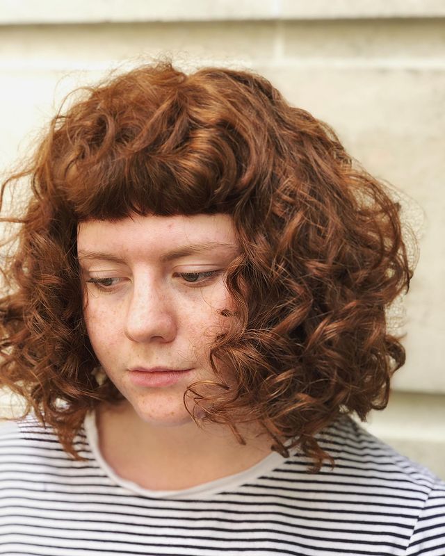 Jovem com expressão levemente sorridente, exibindo seu corte bob, usando blusa branca com listras