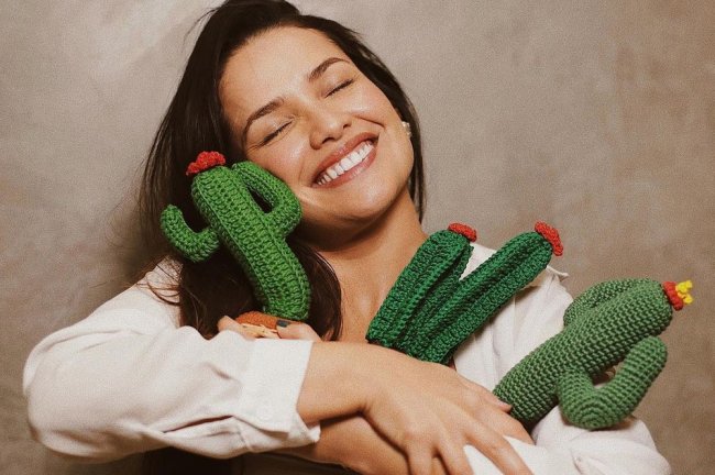 Juliette está sorrindo com os olhos fechados, abraçada com três almofadas de cactos,