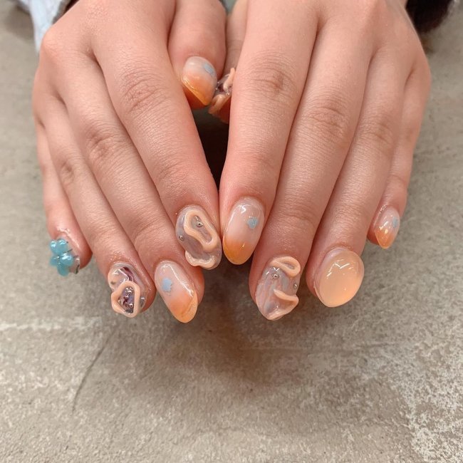 Foto com nail art com gel deixando relevo nas cores laranja e azul.