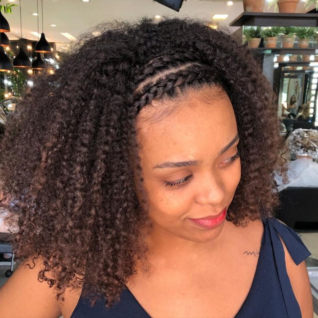 tranca-em-cabelo-cacheado-8 Jovem olhando para baixo, com expressão levemente sorridente usando blusa preta.