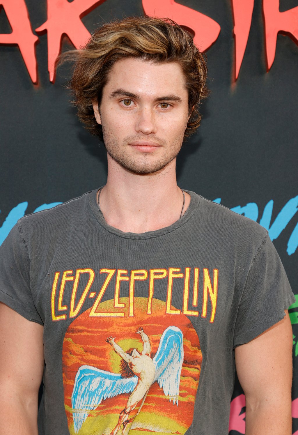 Chase Stokes no carpert da premiere de Rua do Medo com uma camiseta do Led Zeppelin e expressão neutra