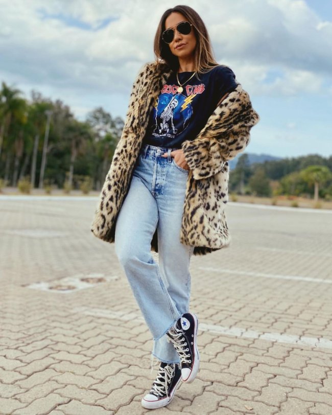 Jovem posando no estacionamento usando calça jeans, camiseta de banda, all star e casaco com estampa animal print.