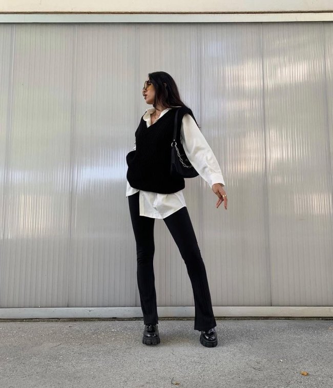 Jovem posando olhando para trás, com camisa branca e colete preto e calça bailarina.