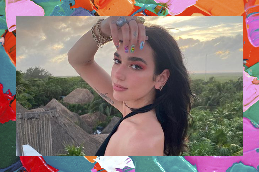 Montagem de foto da Dua Lipa em um fundo cheio de tintas coloridas. Ela está com um vestido preto, olhando para o lado com expressão séria em direção à câmera e com uma das mãos perto do rosto. A foto mostra dos ombros para cima.