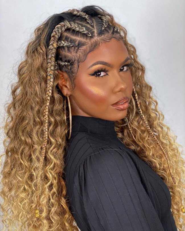 trancinhas em cabelo cacheado Jovem posando com expressão séria, usando blusa de gola alta preta e olhando de lado.