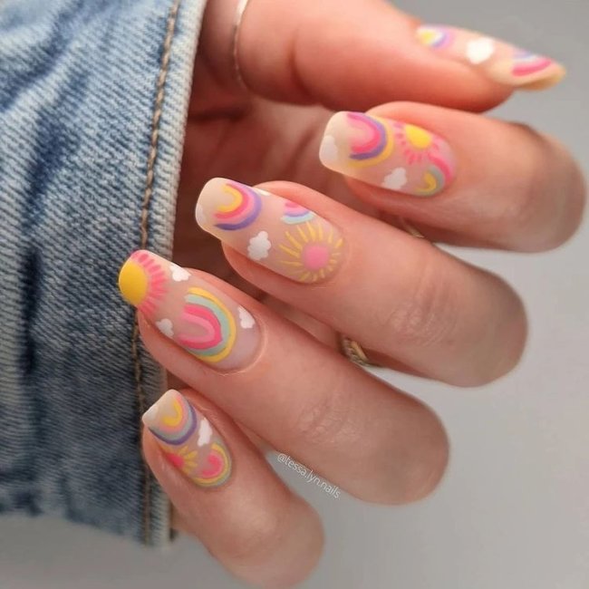 Foto com close nas unhas e tem nail art com desenhos de arco-íris, nas cores, azul, verde, amarelo, lilás e rosa.