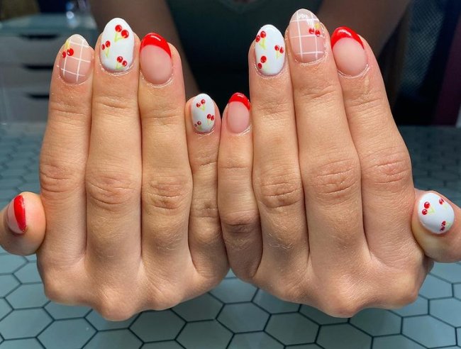 Foto com foco nas mãos exibindo a nail art das unhas. No caso, unhas brancas com detalhes em vermelho e cerejas.