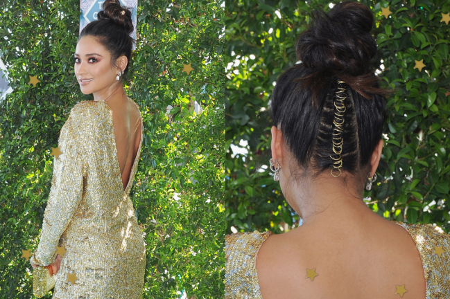 Shay Mitchell no red carpet do TCA posando para mostrar seu visual com vestido dourado e seu penteado.