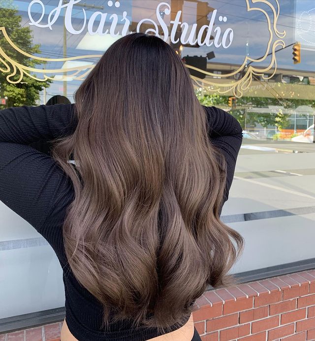 Foto de uma mulher de costas mostrando o cabelo. Ela usa uma blusa de manga longa preta e mostra o cabelo longo castanho acinzentado.