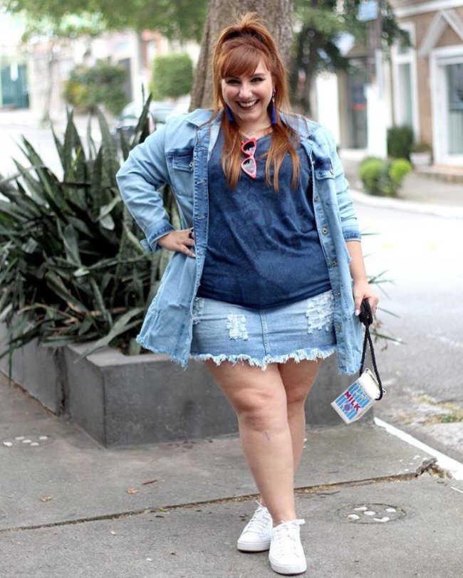 look com saia jeans Jovem posando com uma das mãos na cintura usando blusinha e saia. Ela está sorridente.