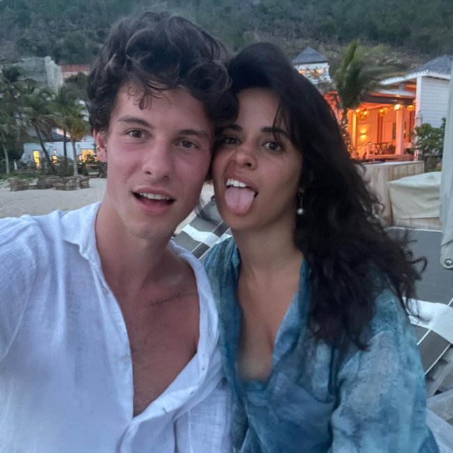 shawn mendes camila cabello Shawn Mendes e Camila Cabello em selfie na praia tirada pelo cantor; os dois estão com os cabelos bagunçados e fazendo careta; Shawn usa uma camisa branca aberta e Camila está com uma saída de praia azul com detalhes brancos mostrando a língua