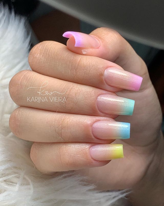 Foto de uma mão com foco nas unhas decoradas no estilo baby boomer nos tons de liás, rosa, azul claro, azul escuro e amarelo.