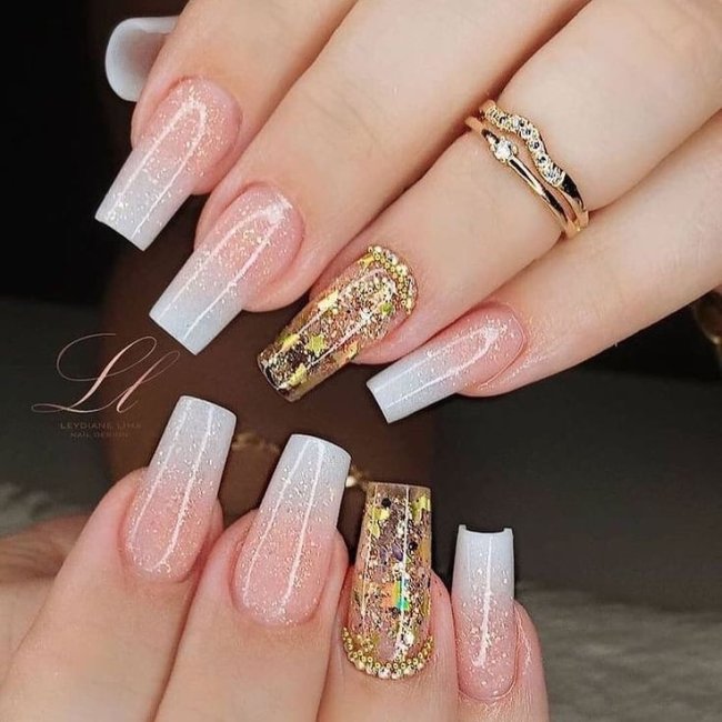 Foto de unhas pintadas com a técnica baby boomer na cor branca, o dedo anelar está com um anel dourado e decoração dourada na unha.