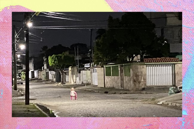 Foto de uma boneca sentada em uma cadeira de plástico, posicionada no centro de uma encruzilhada. É noite.